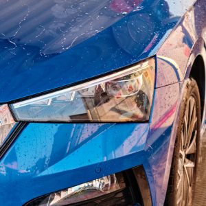 Close up hood and headlight of a blue car in a drops of water after car washing. Clean car after