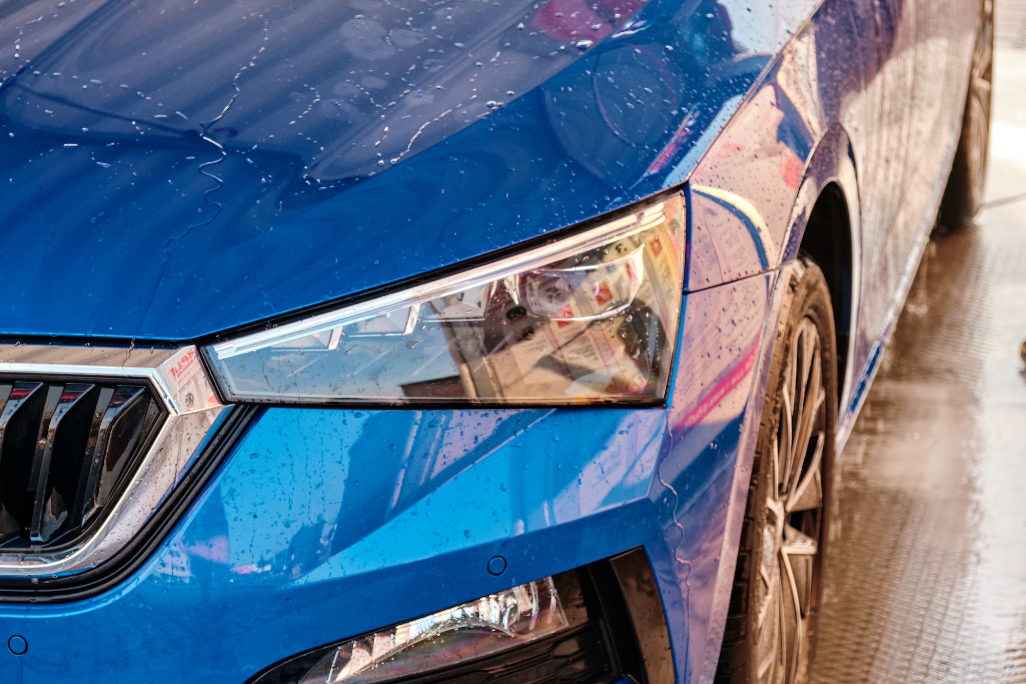 Close up hood and headlight of a blue car in a drops of water after car washing. Clean car after
